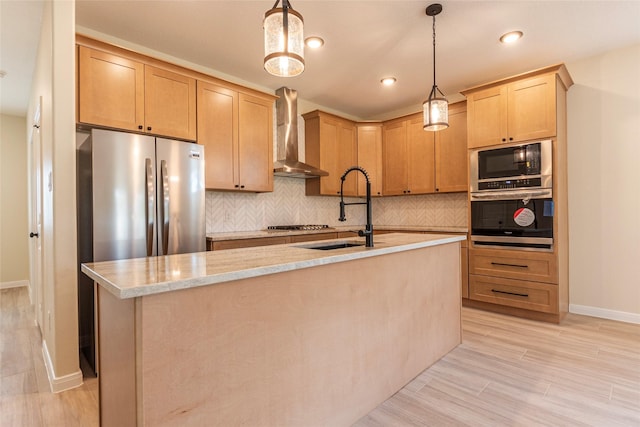 kitchen featuring backsplash, appliances with stainless steel finishes, wall chimney range hood, and a sink