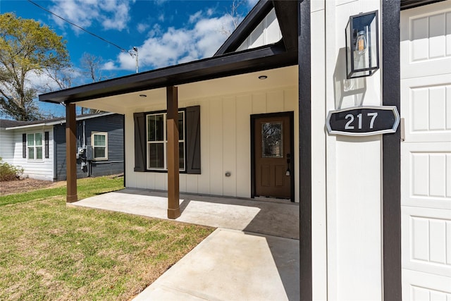 view of exterior entry featuring a yard, covered porch, and board and batten siding