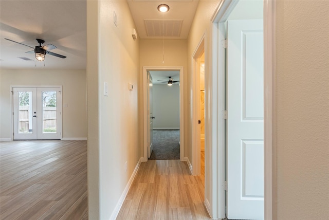 hall with attic access, light wood-style floors, visible vents, and baseboards