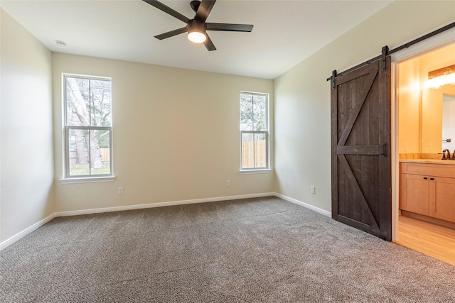 unfurnished bedroom featuring baseboards, a sink, light carpet, a barn door, and connected bathroom