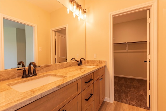 bathroom featuring double vanity, a spacious closet, wood finished floors, and a sink