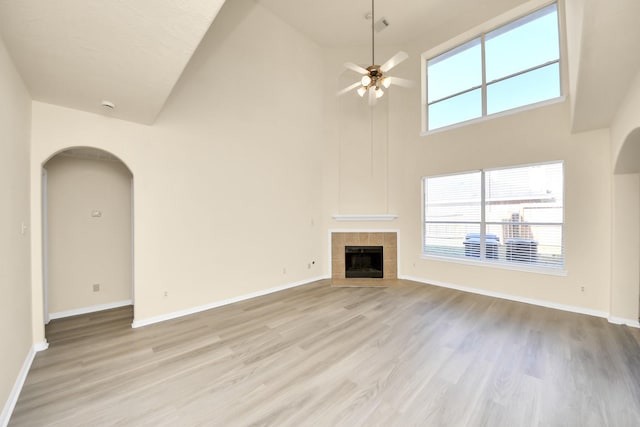 unfurnished living room with light wood finished floors, baseboards, ceiling fan, a tiled fireplace, and arched walkways