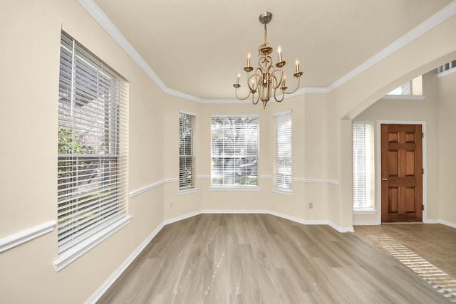 unfurnished dining area featuring a notable chandelier, crown molding, baseboards, and wood finished floors