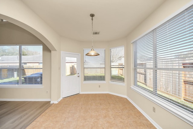 unfurnished dining area with light tile patterned floors, baseboards, arched walkways, and visible vents