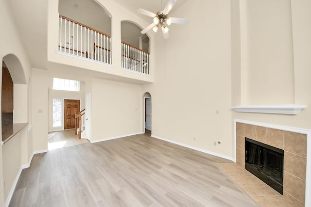 unfurnished living room with wood finished floors, baseboards, arched walkways, ceiling fan, and a tiled fireplace