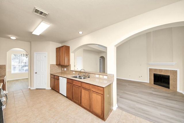 kitchen with visible vents, backsplash, white dishwasher, brown cabinetry, and a sink