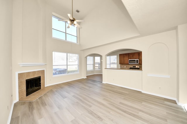 unfurnished living room with a tiled fireplace, baseboards, light wood-type flooring, and a ceiling fan