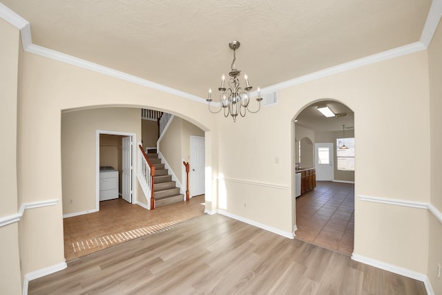 unfurnished dining area featuring washer / clothes dryer, arched walkways, an inviting chandelier, light wood finished floors, and stairs