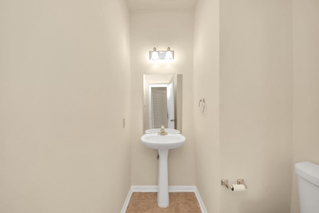 half bath featuring tile patterned flooring, toilet, and baseboards