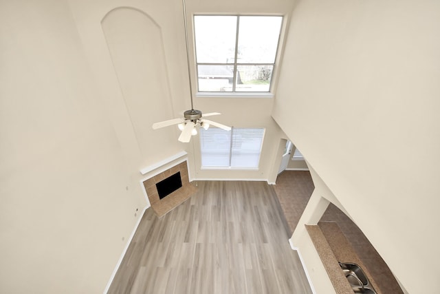 unfurnished living room with baseboards, a tile fireplace, a high ceiling, light wood-style floors, and a ceiling fan