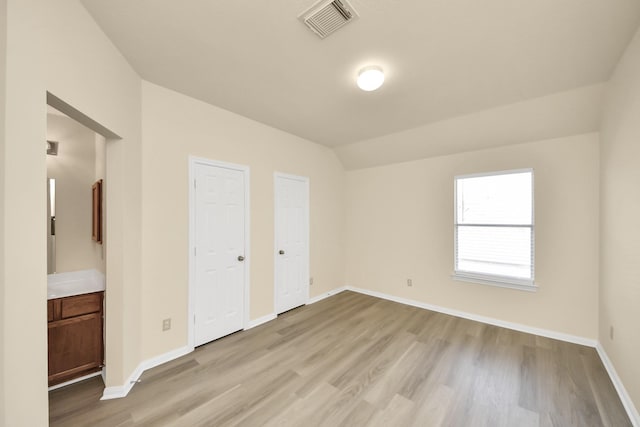 unfurnished bedroom with visible vents, light wood-style flooring, baseboards, and vaulted ceiling