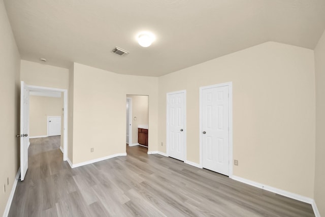 unfurnished bedroom with visible vents, wood finished floors, baseboards, and two closets