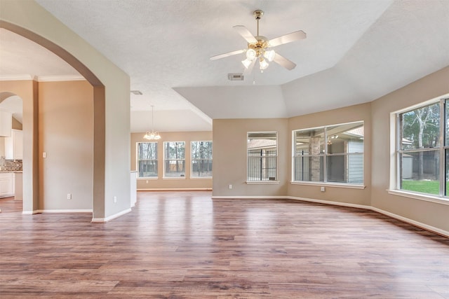 empty room with wood finished floors, baseboards, lofted ceiling, arched walkways, and ceiling fan with notable chandelier