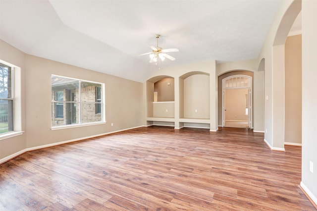 unfurnished room featuring arched walkways, baseboards, a ceiling fan, and wood finished floors