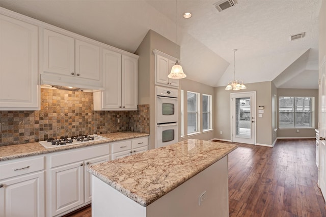 kitchen with white appliances, visible vents, under cabinet range hood, and vaulted ceiling