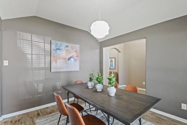 dining area with baseboards, arched walkways, wood finished floors, and vaulted ceiling