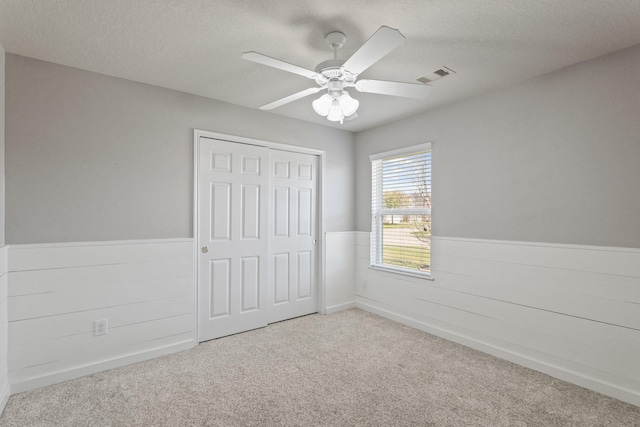 unfurnished bedroom with visible vents, wainscoting, a textured ceiling, and carpet floors