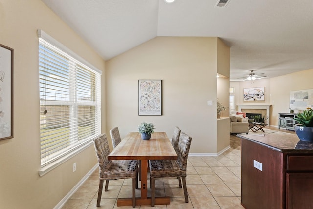 dining area with baseboards, lofted ceiling, light tile patterned floors, a glass covered fireplace, and a ceiling fan