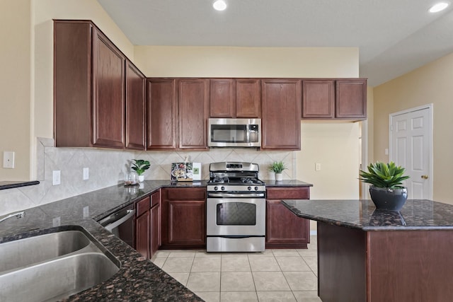 kitchen with backsplash, light tile patterned floors, dark stone countertops, appliances with stainless steel finishes, and a sink