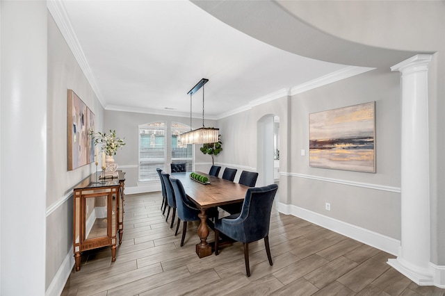 dining space featuring baseboards, wood finish floors, decorative columns, arched walkways, and crown molding