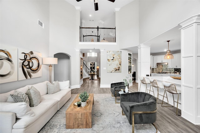 living room with decorative columns, visible vents, wood finished floors, and a ceiling fan