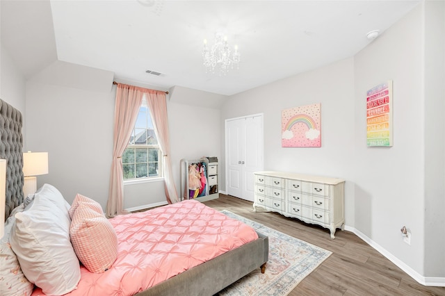 bedroom with wood finished floors, visible vents, baseboards, lofted ceiling, and a notable chandelier