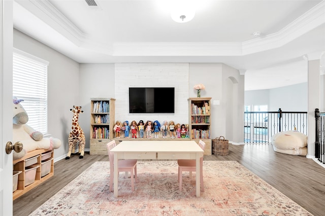 rec room with a tray ceiling, wood finished floors, baseboards, and ornamental molding