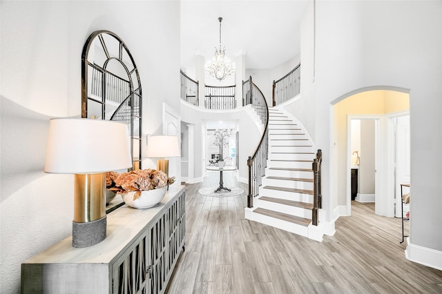 foyer with stairway, arched walkways, a chandelier, and light wood finished floors