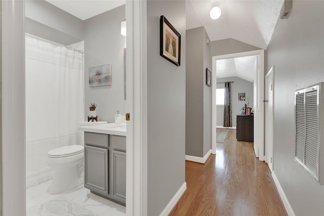 hall featuring visible vents, baseboards, light wood-style floors, and vaulted ceiling