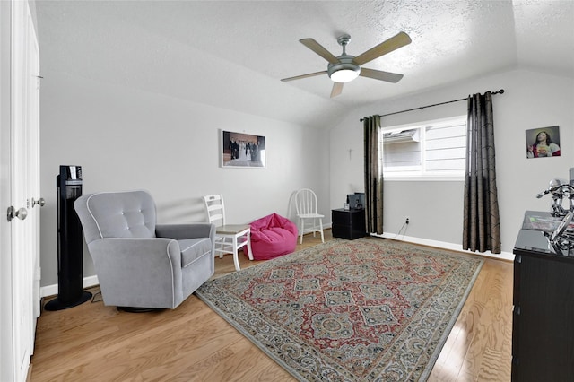 living area featuring lofted ceiling, a ceiling fan, light wood finished floors, and a textured ceiling