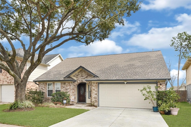 view of front facade featuring a front yard, driveway, an attached garage, a shingled roof, and brick siding