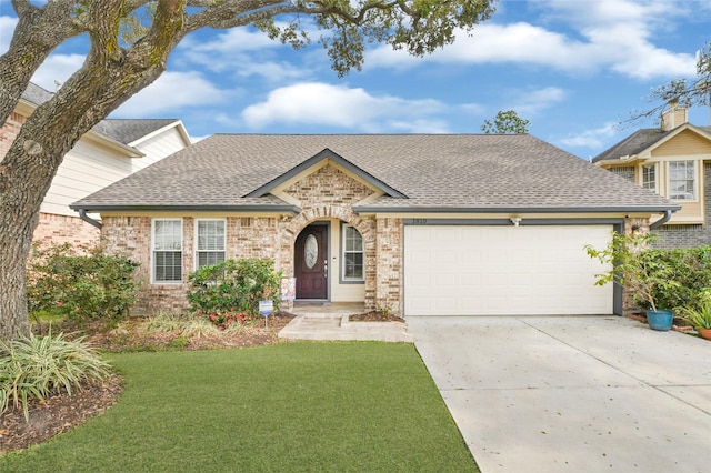 view of front facade with an attached garage, a shingled roof, concrete driveway, a front lawn, and brick siding