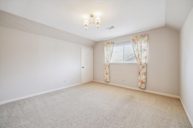 empty room featuring visible vents, a textured ceiling, carpet, and vaulted ceiling