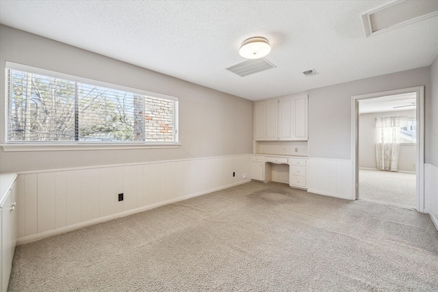 spare room featuring visible vents, light colored carpet, wainscoting, and a textured ceiling