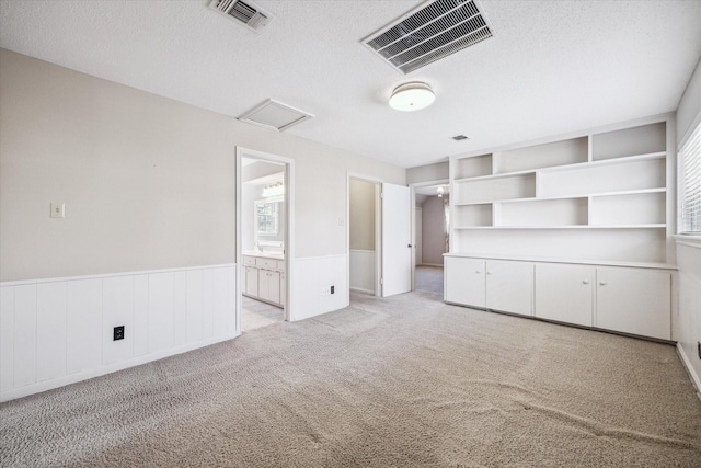 unfurnished bedroom with a wainscoted wall, visible vents, attic access, a textured ceiling, and light colored carpet