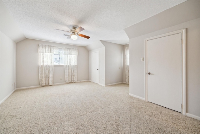 spare room with baseboards, lofted ceiling, light carpet, a textured ceiling, and a ceiling fan