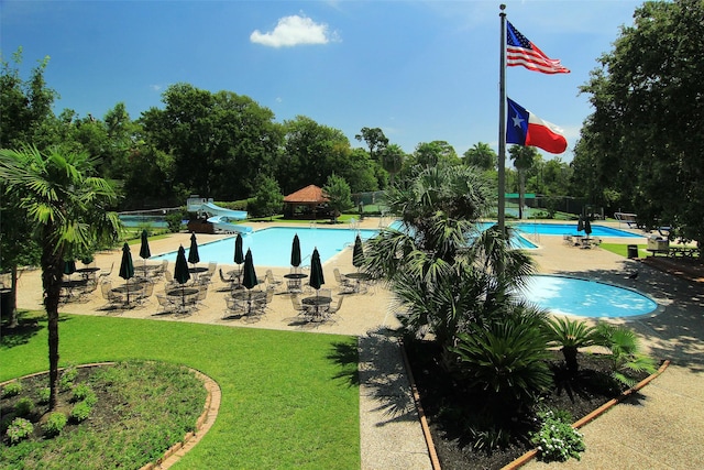 pool with a patio area, a lawn, a water slide, and fence