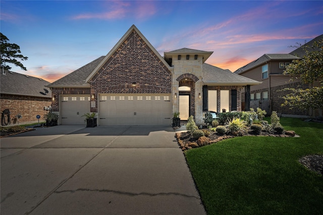 french country style house featuring an attached garage, a shingled roof, concrete driveway, stone siding, and a lawn