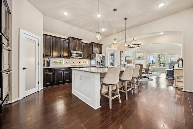 kitchen with dark wood-style flooring, dark brown cabinetry, open floor plan, appliances with stainless steel finishes, and tasteful backsplash