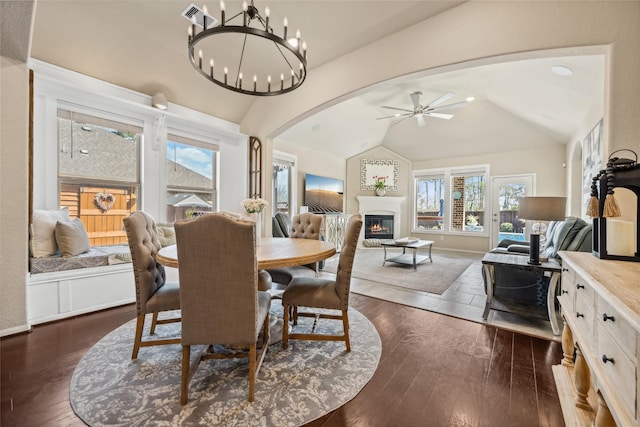 dining area featuring dark wood-style floors, a glass covered fireplace, arched walkways, and vaulted ceiling