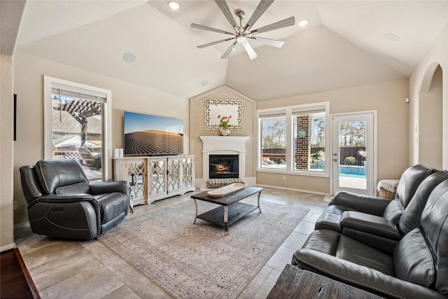 living area with baseboards, a glass covered fireplace, a ceiling fan, and lofted ceiling