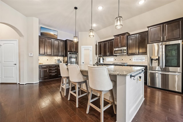 kitchen with a sink, dark wood finished floors, stainless steel appliances, arched walkways, and dark brown cabinetry