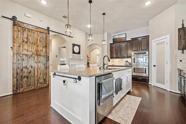 kitchen with a sink, stainless steel appliances, arched walkways, and tasteful backsplash