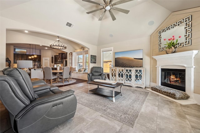 living area with visible vents, arched walkways, a glass covered fireplace, high vaulted ceiling, and a ceiling fan