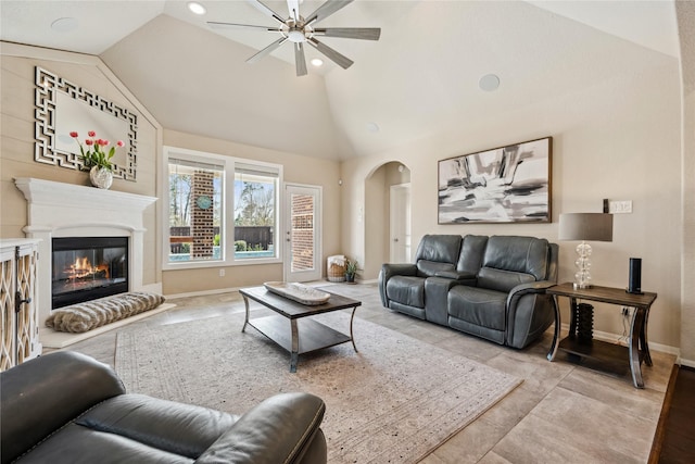 living room with a glass covered fireplace, vaulted ceiling, a ceiling fan, and arched walkways