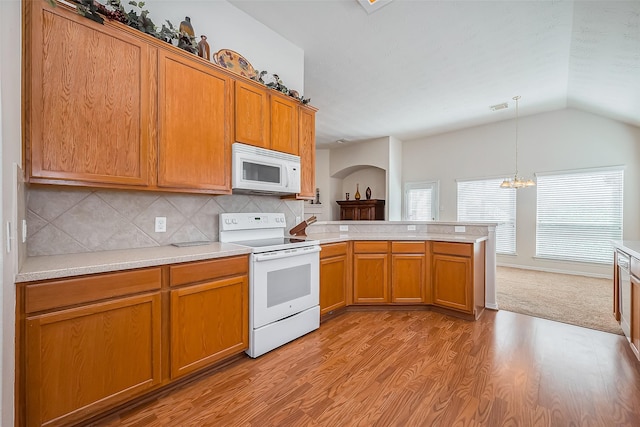 kitchen featuring brown cabinetry, white appliances, a peninsula, and vaulted ceiling