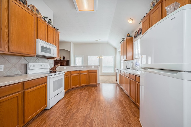 kitchen with white appliances, a peninsula, lofted ceiling, light countertops, and brown cabinets