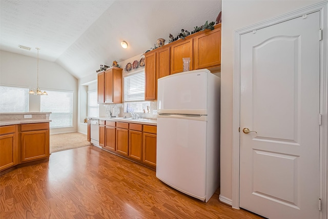 kitchen with white appliances, light countertops, brown cabinets, and vaulted ceiling