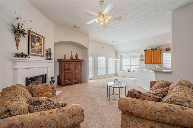 living room featuring a fireplace, vaulted ceiling, a textured ceiling, ceiling fan with notable chandelier, and light colored carpet