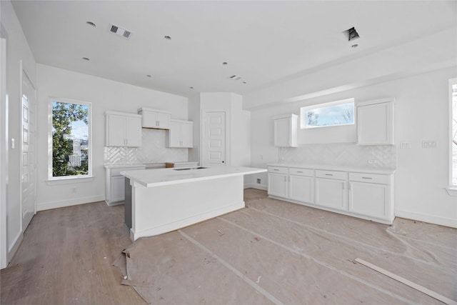 kitchen featuring baseboards, visible vents, a kitchen island, white cabinetry, and tasteful backsplash